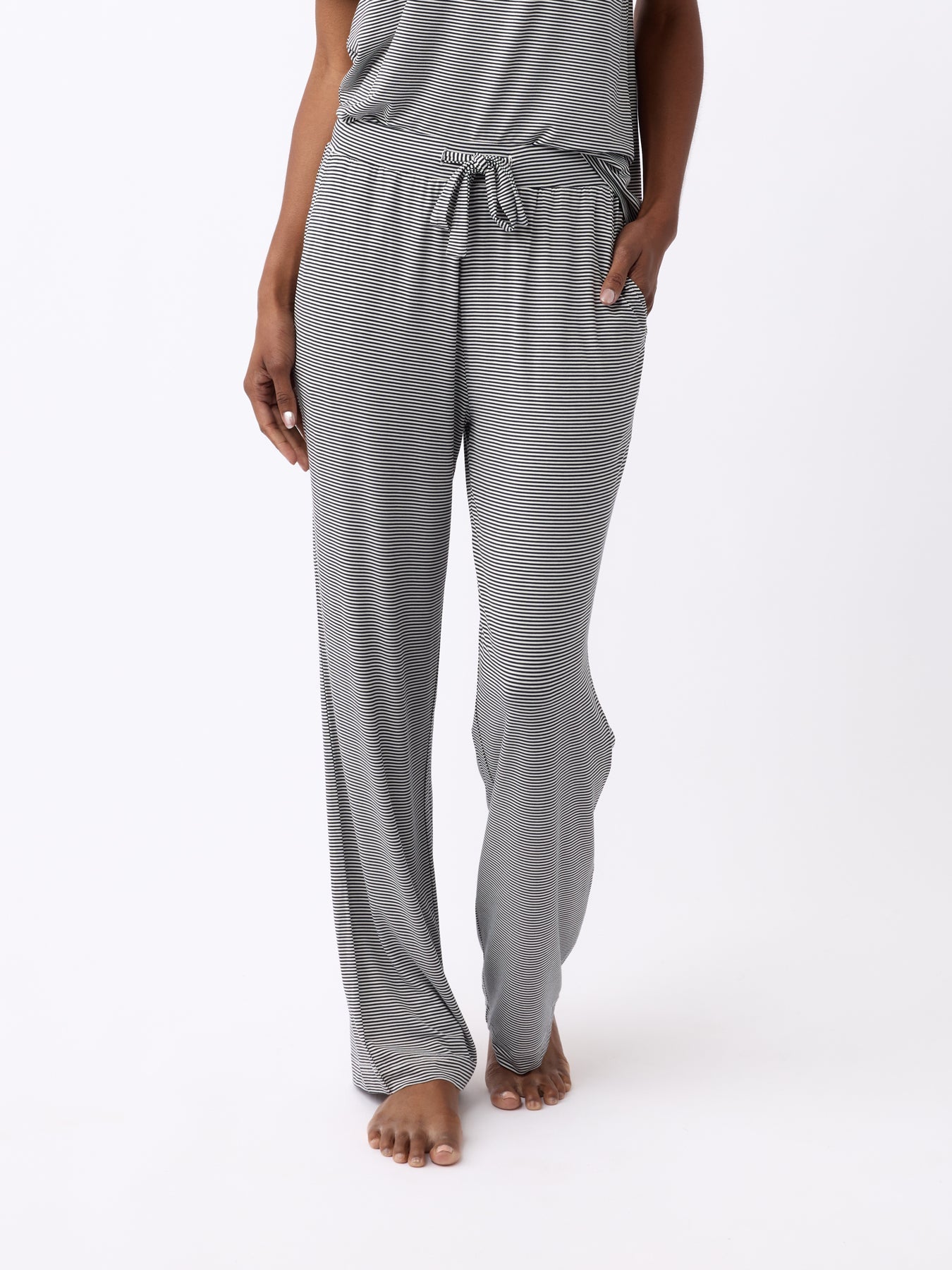 A person is standing barefoot against a white background, wearing Cozy Earth's Women's Bamboo Stretch-Knit Pant in a gray-striped design with a drawstring waist and relaxed fit for comfort. |Color:Eclipse Mini Stripe