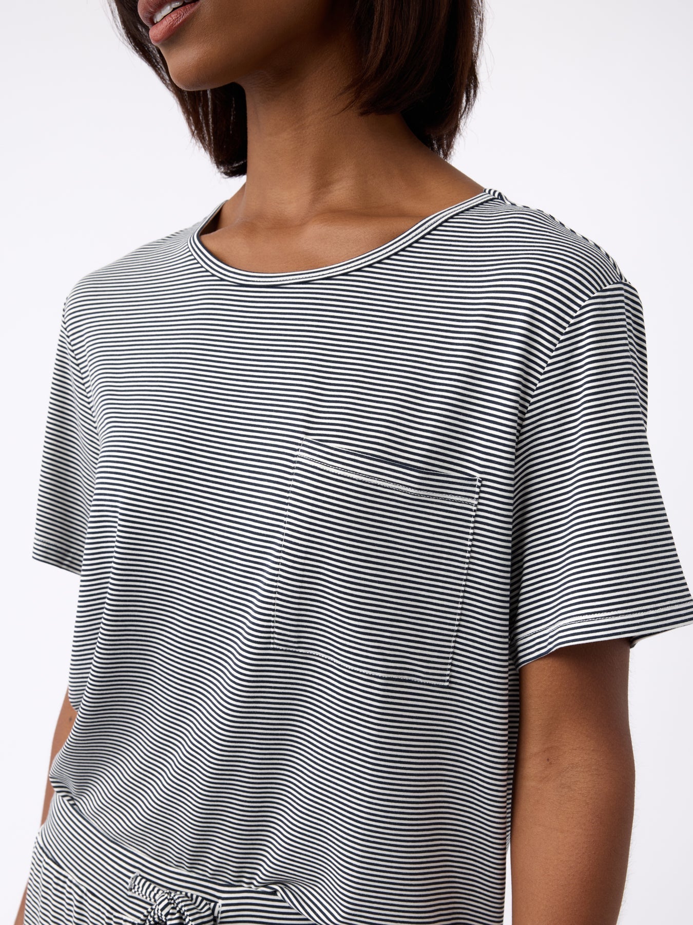 A person wearing Cozy Earth's Women's Bamboo Stretch-Knit Lounge Tee in black and white stripes with a pocket, featuring short sleeves and a round neckline against a plain white background. |Color:Eclipse Mini Stripe
