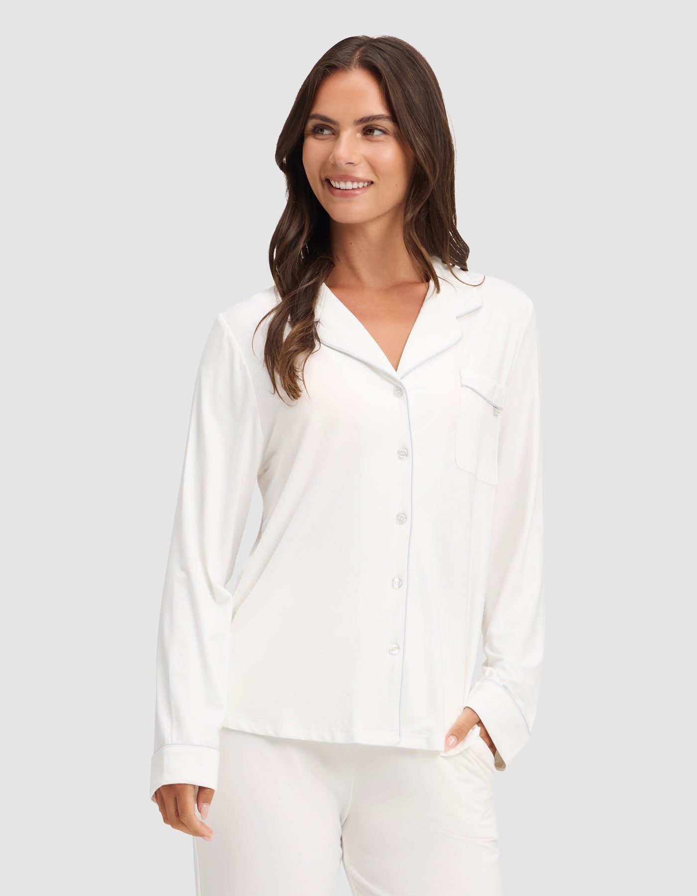A woman smiles against a light gray background wearing HIDE's Women's Bamboo Stretch-Knit Long Sleeve Pajama Top with matching pants. |Color:Ivory