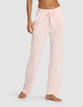 A woman wears Cozy Earth Women's Bamboo Stretch-Knit Pant in light pink, featuring a loose fit, elastic waistband, and drawstring, standing barefoot against a plain background.|Color:Blossom