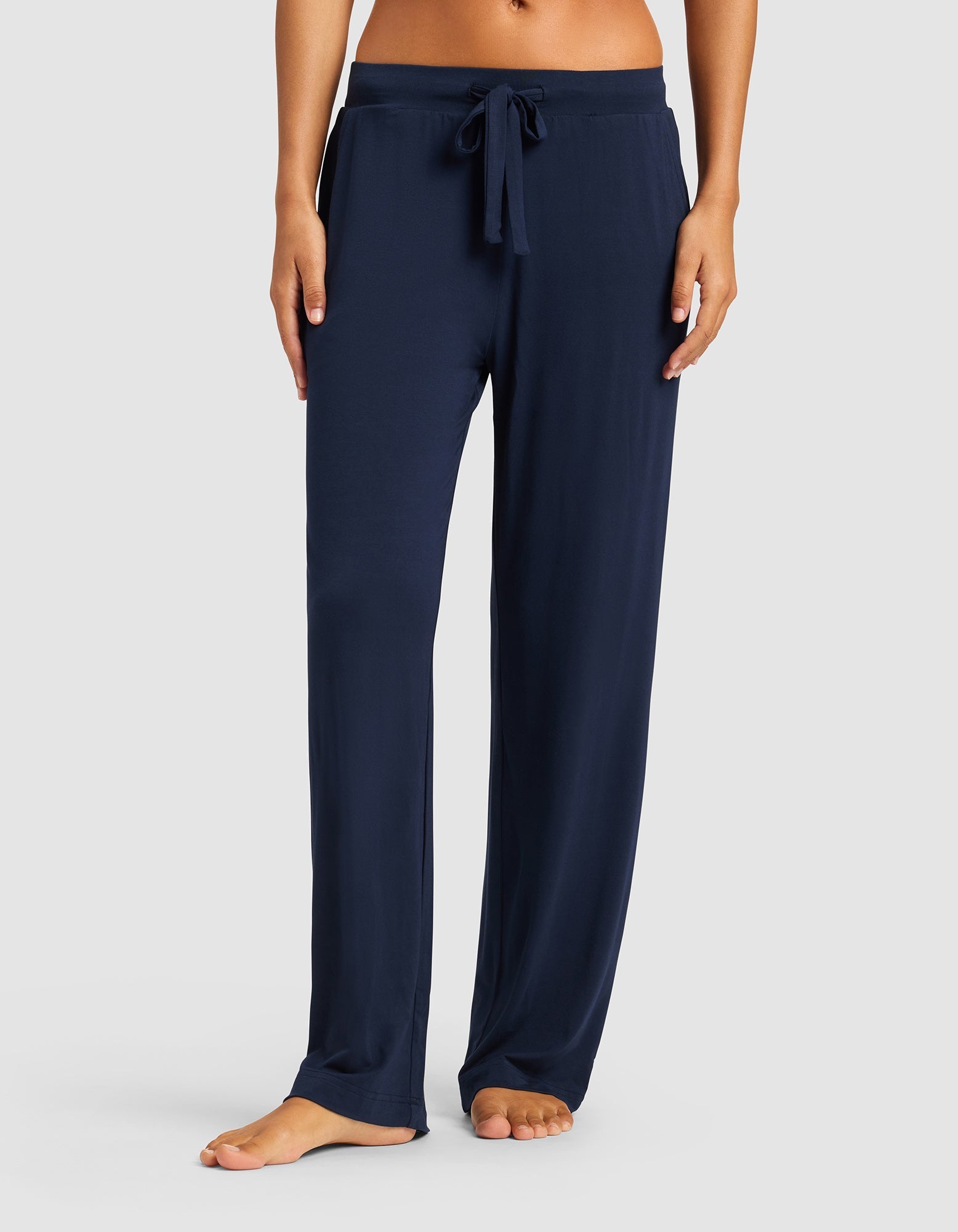Model wears Cozy Earth Women’s Bamboo Stretch-Knit Pant in navy blue, featuring a loose fit and drawstring waist, shown barefoot with only the lower torso and legs visible against a light gray background.|Color:Navy
